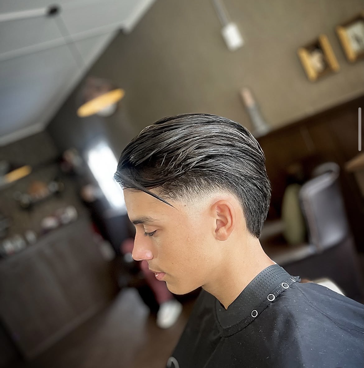 Zijaanzicht van een strak achterovergekamd kapsel met een fade, in de zaak van Barboer
